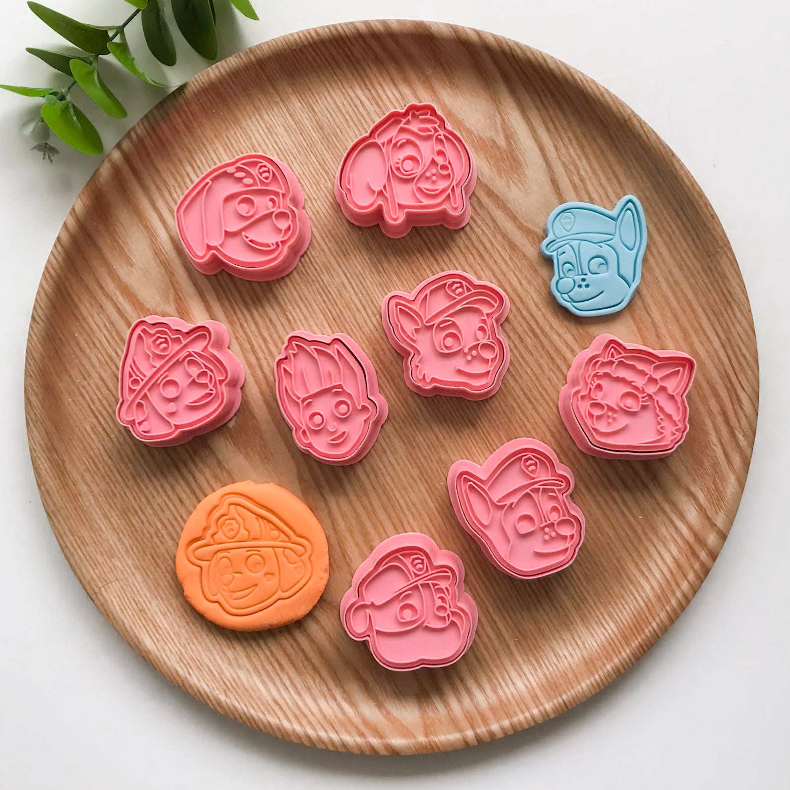 A set of colorful paw patrol face-shaped cutters for crafting, displayed on a wooden plate. Each cutter has a cartoonish puppy face design