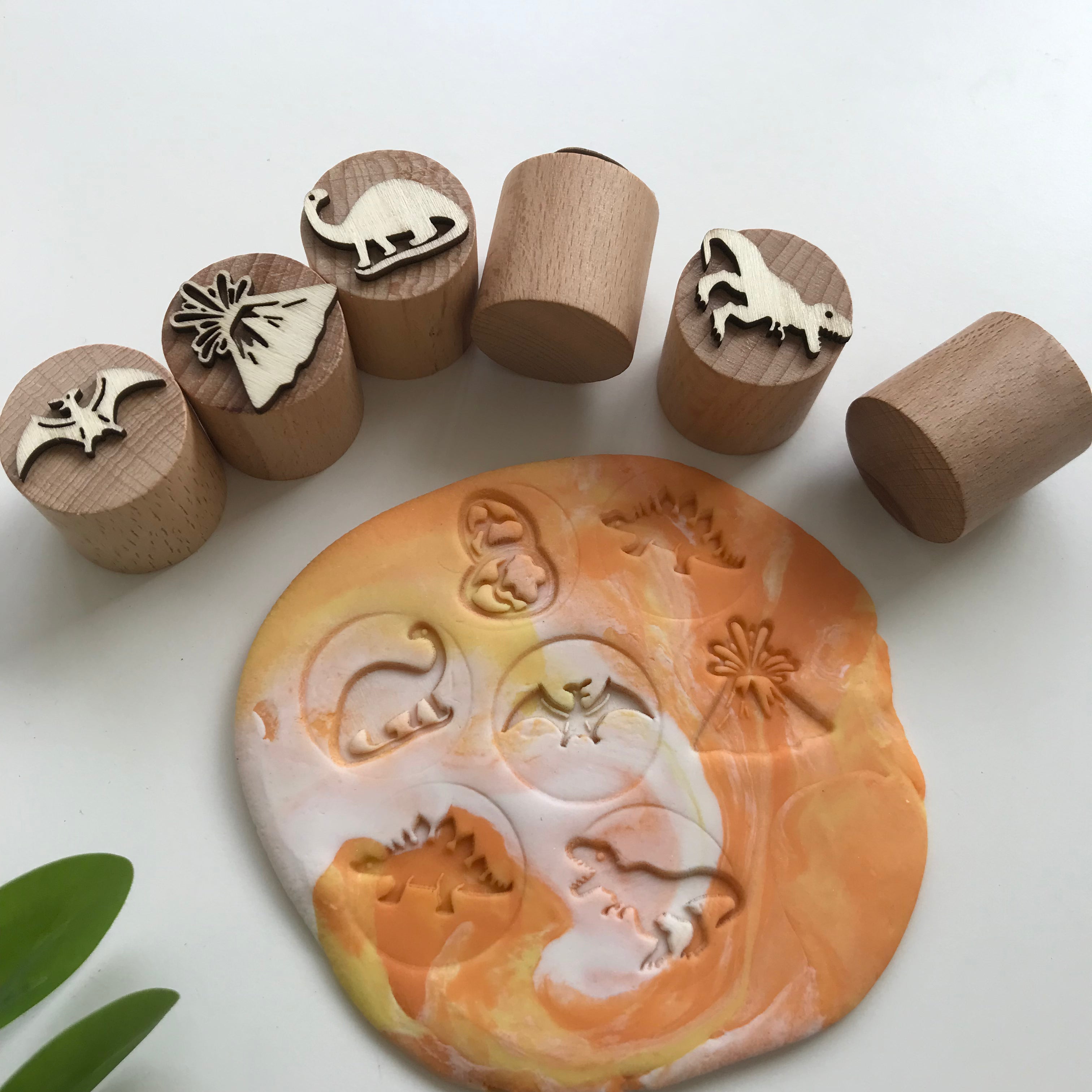 A set of 6 dinosaur themed wooden playdough stampers. Marbled white and orange playdough in the middle with all the outlines of the playdough stamps