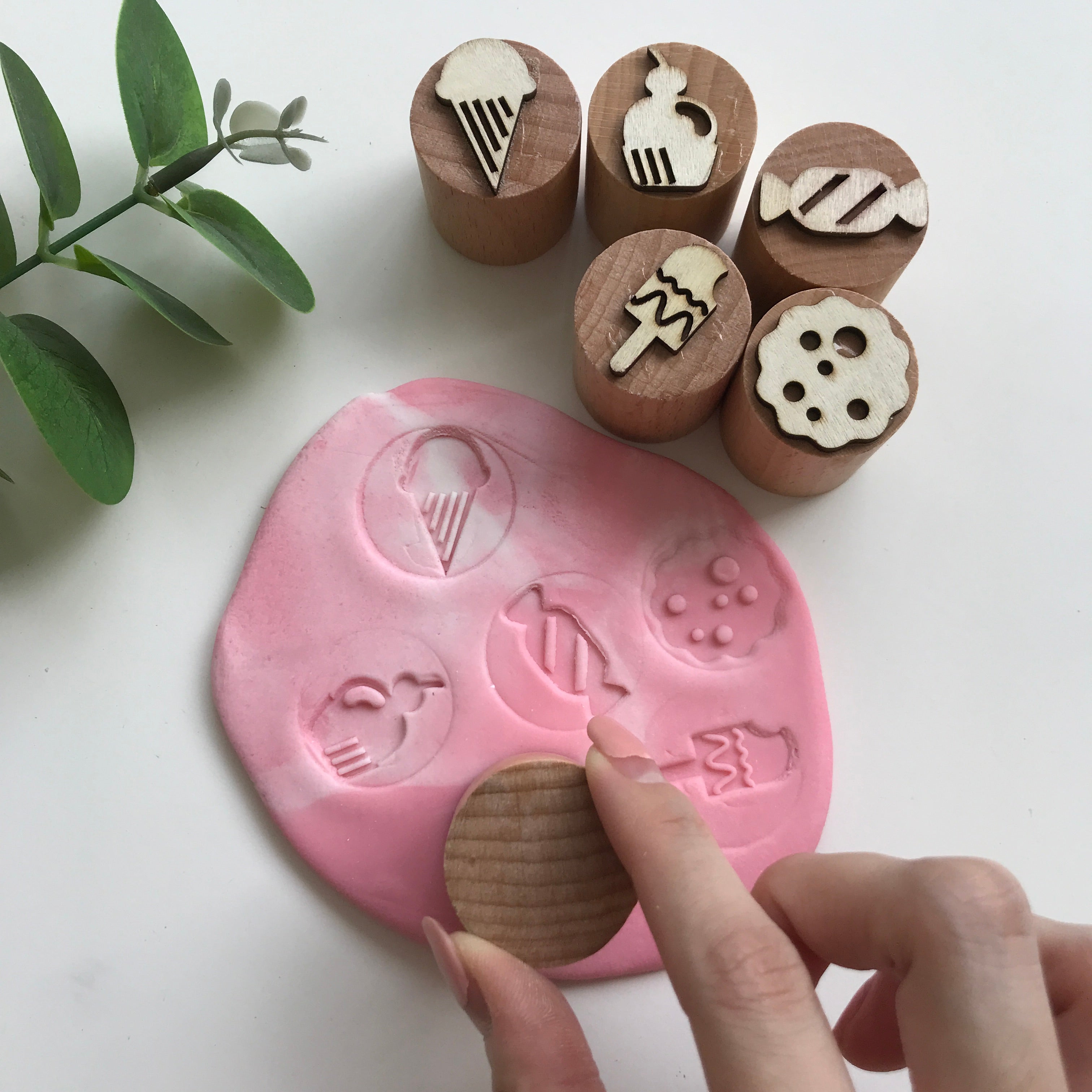 Hand holding on to a wooden chop to make an imprint on the pink playdough