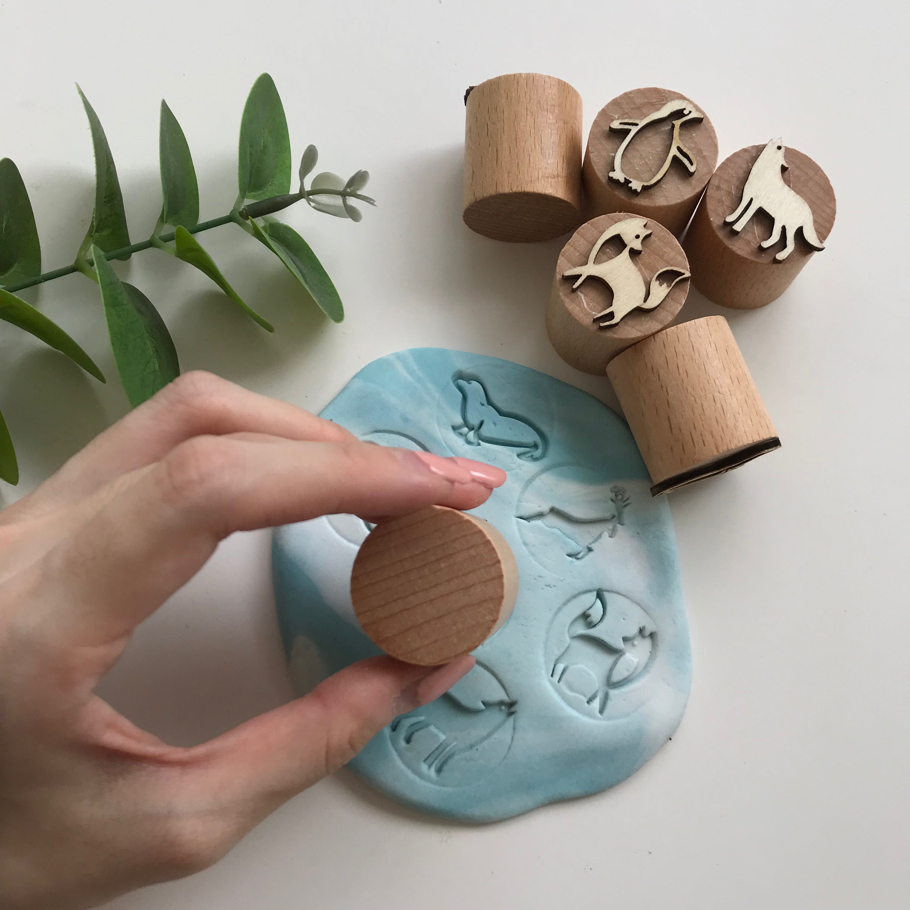 A hand holding a playdough stamper pressing against a piece of blue and white playdough to make an imprint.