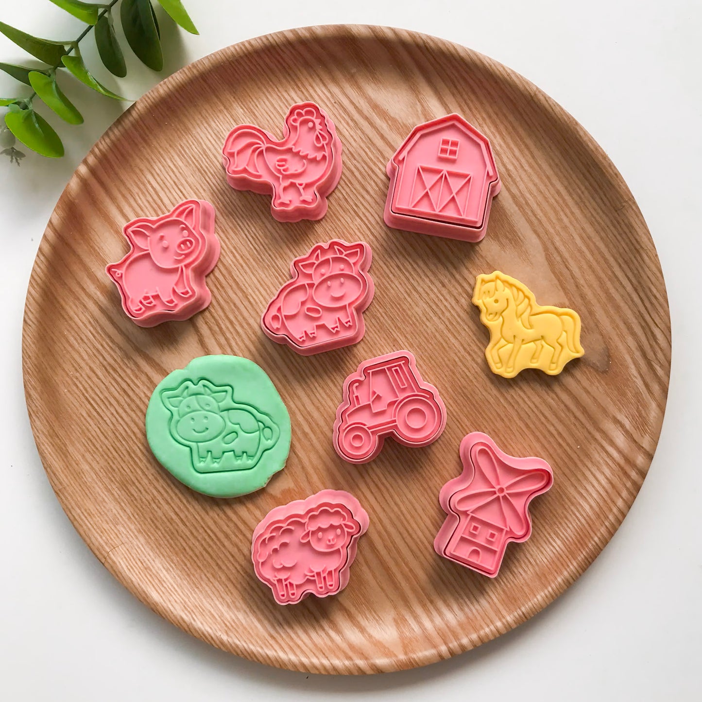 A set of colorful farm animal-themed playdough cutters and stampers made of plastic, displayed on a wooden board.