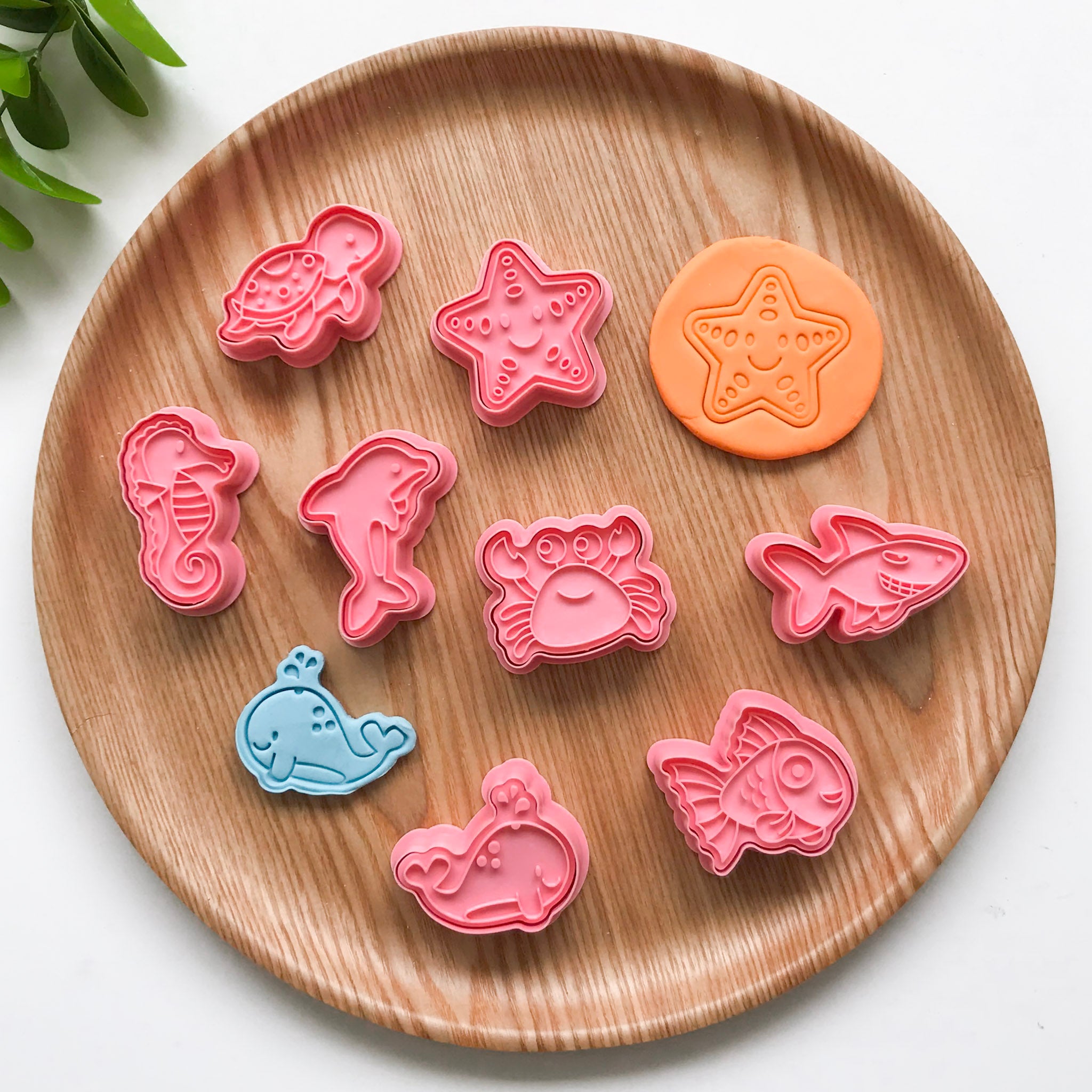 A set of colorful ocean animal-themed playdough cutters displayed on a wooden plate. The animals featured are a turtle, seahorse, dolphin, starfish, whale, crab, shark and a fish