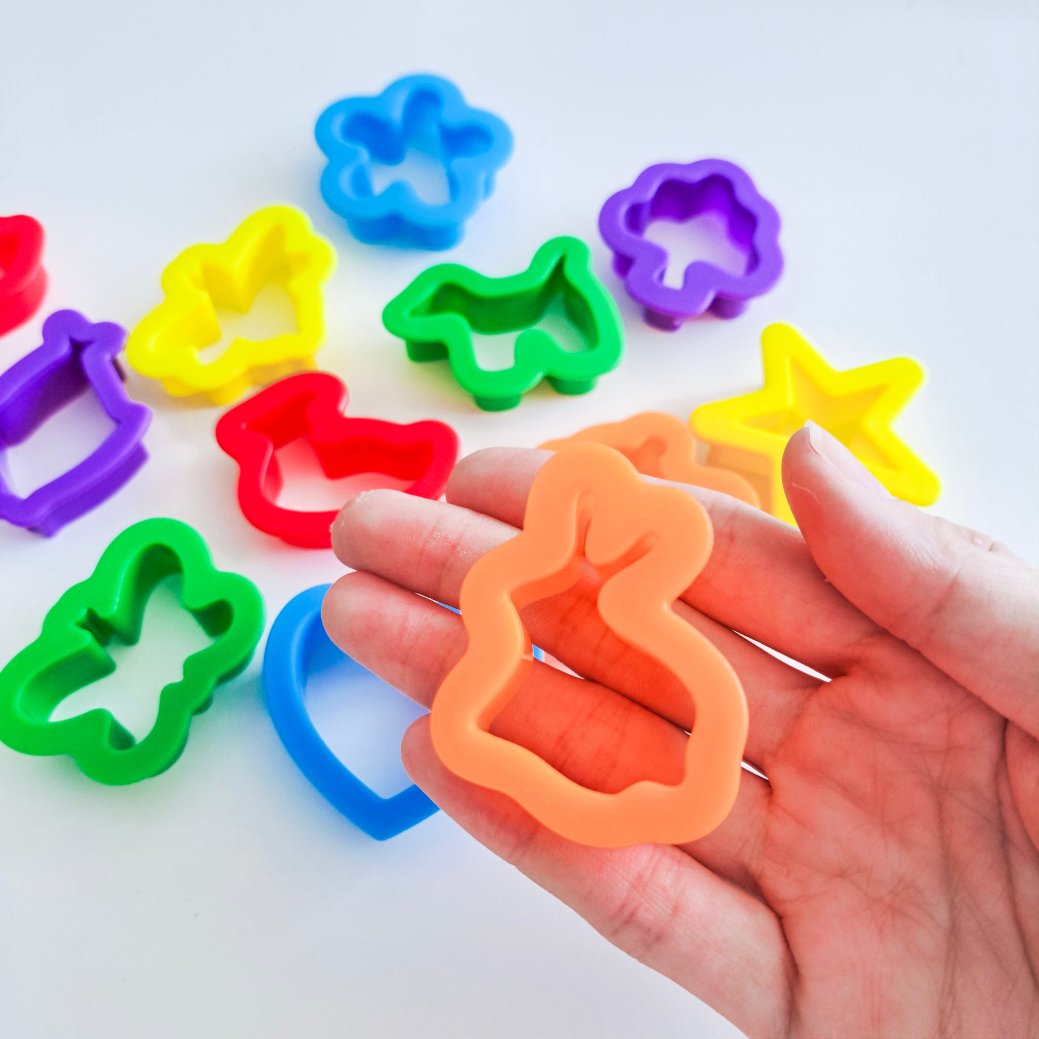 Hand holding a rabbit playdough miniature cutter, against a backdrop where there are other playdough cutters