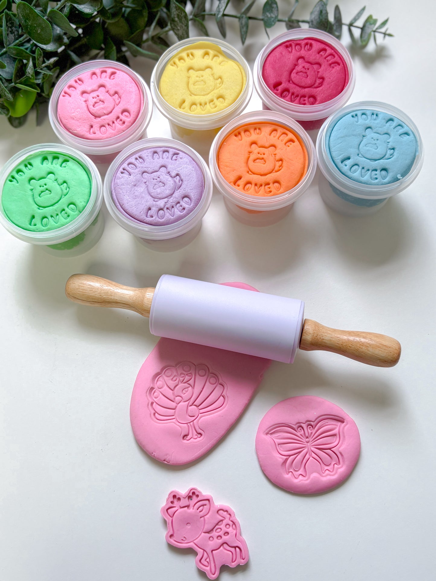 Set of colorful playdough tubs and stampers with a rolling pin and stamps on a white surface.