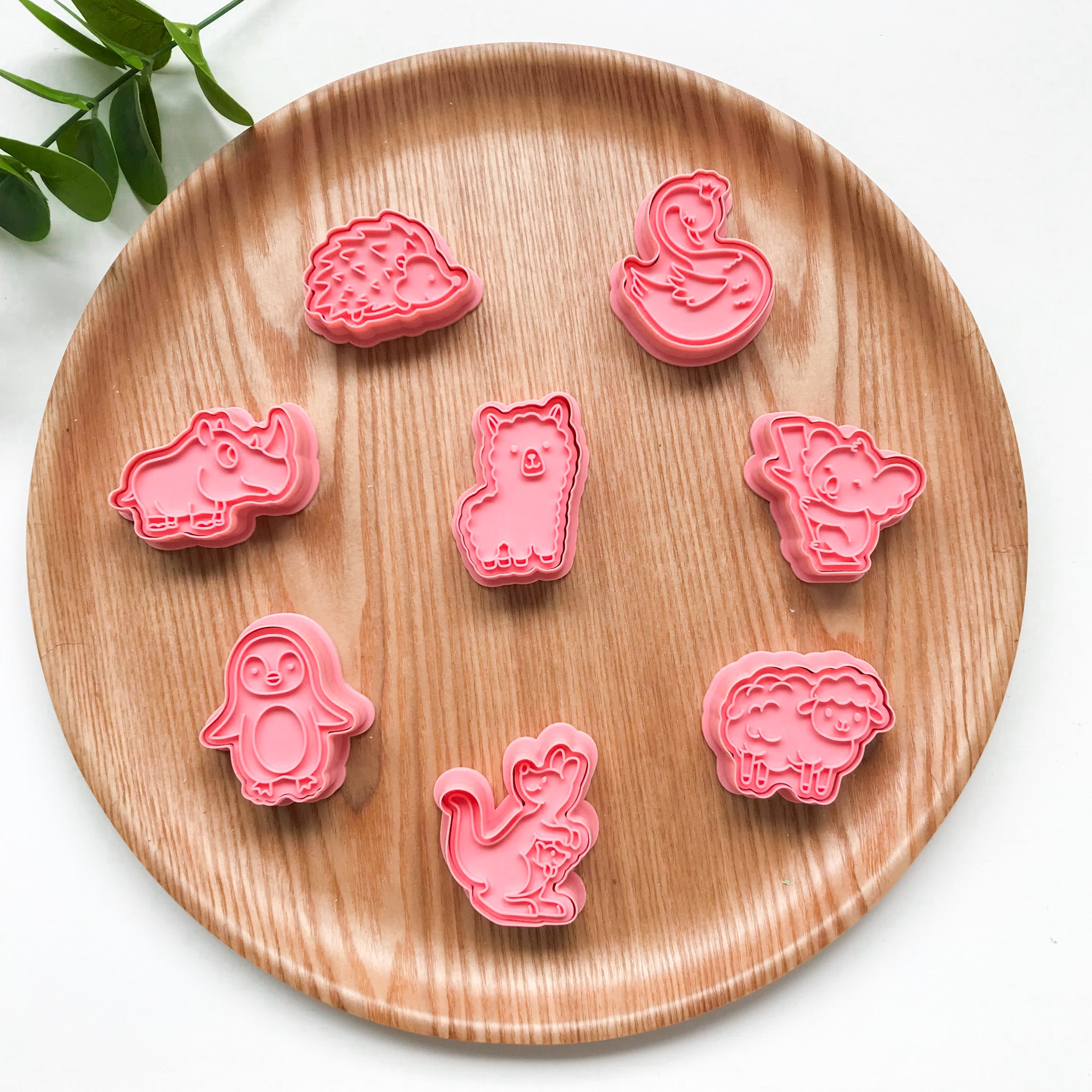 A collection of pink-colored Australian animal-themed playdough cutters arranged on a wooden plate.