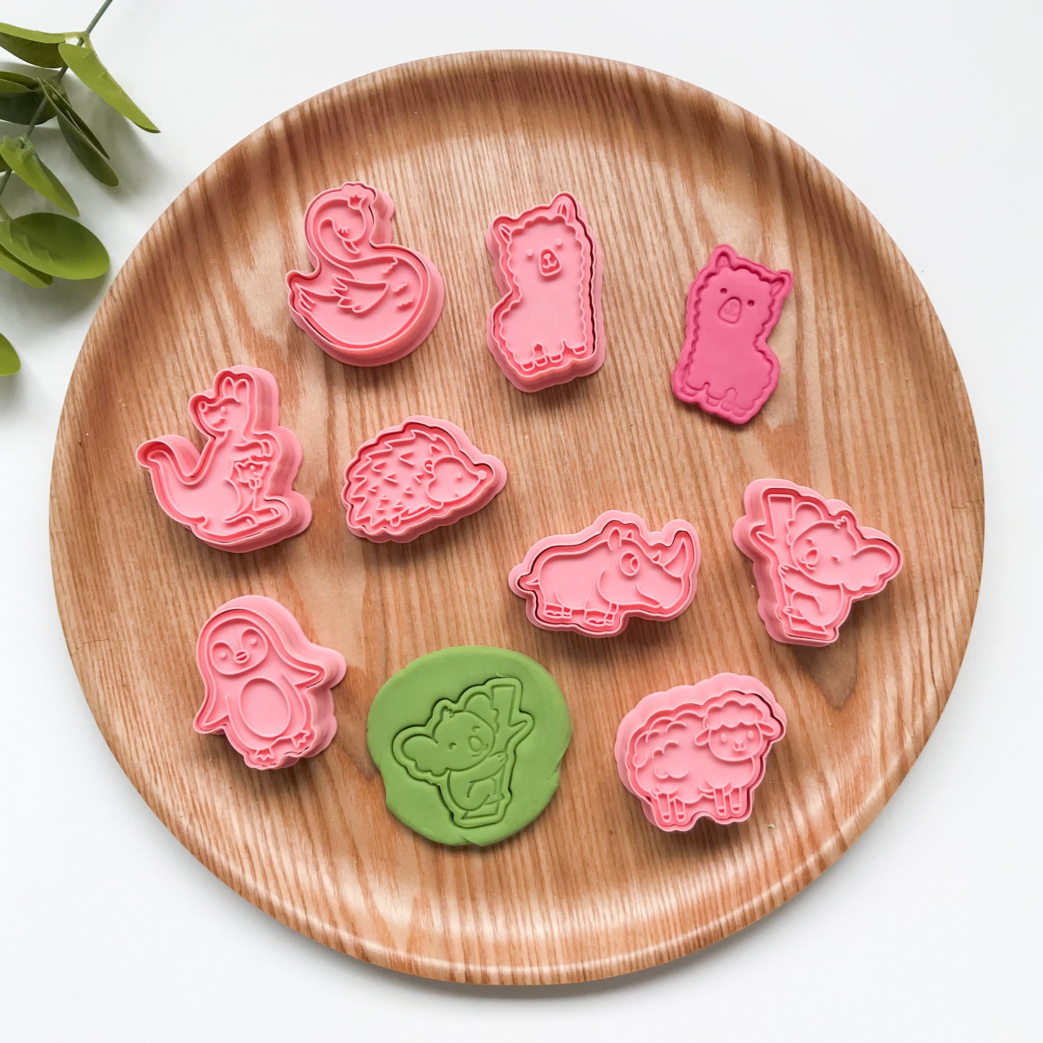 A collection of pink-colored Australian animal-themed playdough cutters arranged on a wooden plate.