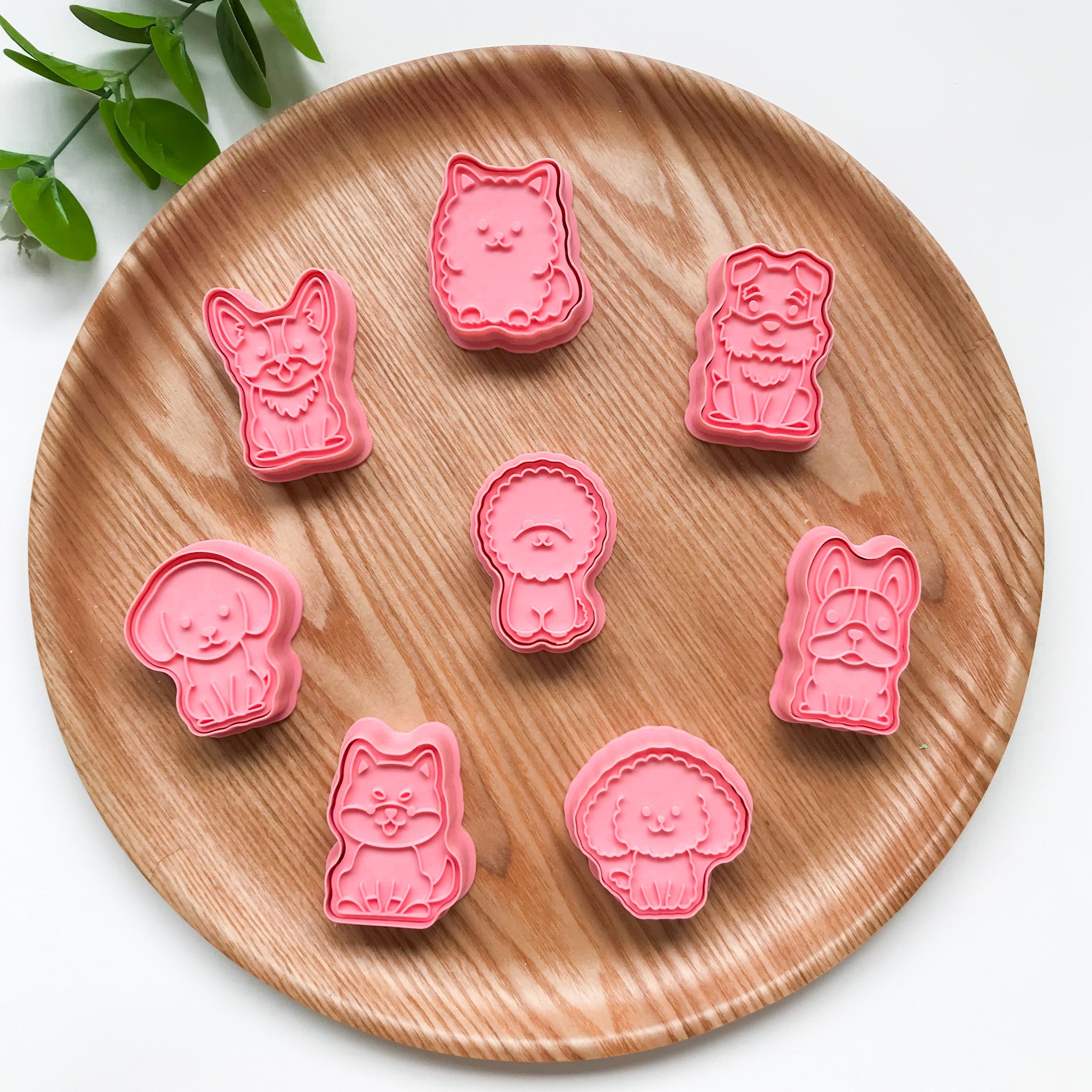 A collection of pink-colored Dog themed playdough cutters arranged on a wooden plate. Features 8 different breeds of dogs