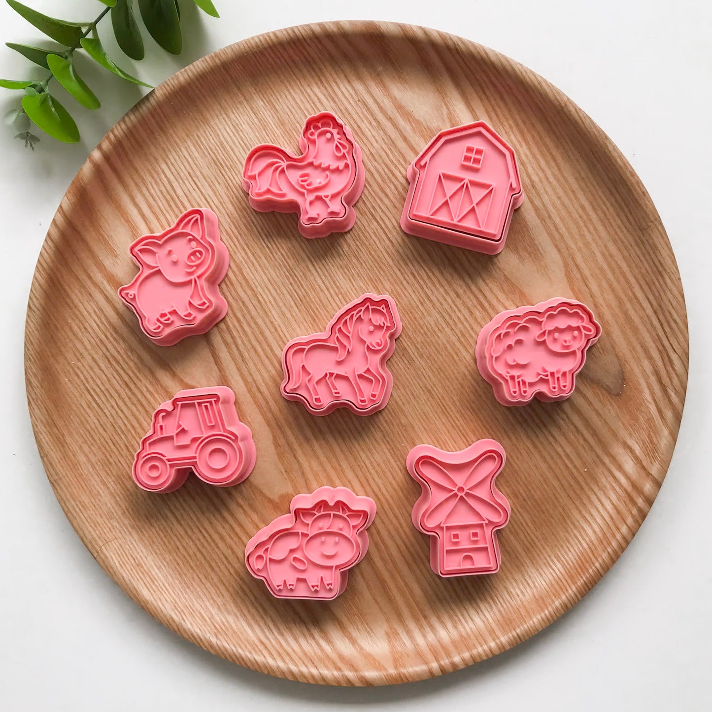 A set of colorful farm animal-themed playdough cutters and stampers made of plastic, displayed on a wooden board.
