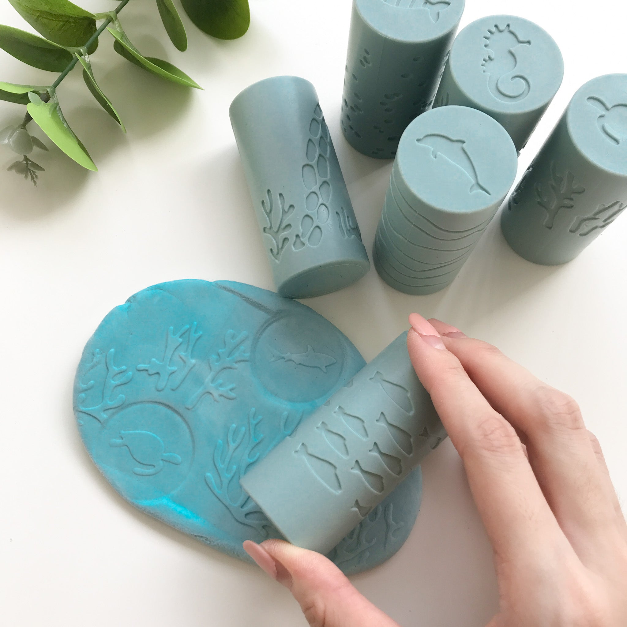 A hand rolling the silicone playdough roller along the piece of blue playdough to make coral and fish imprints