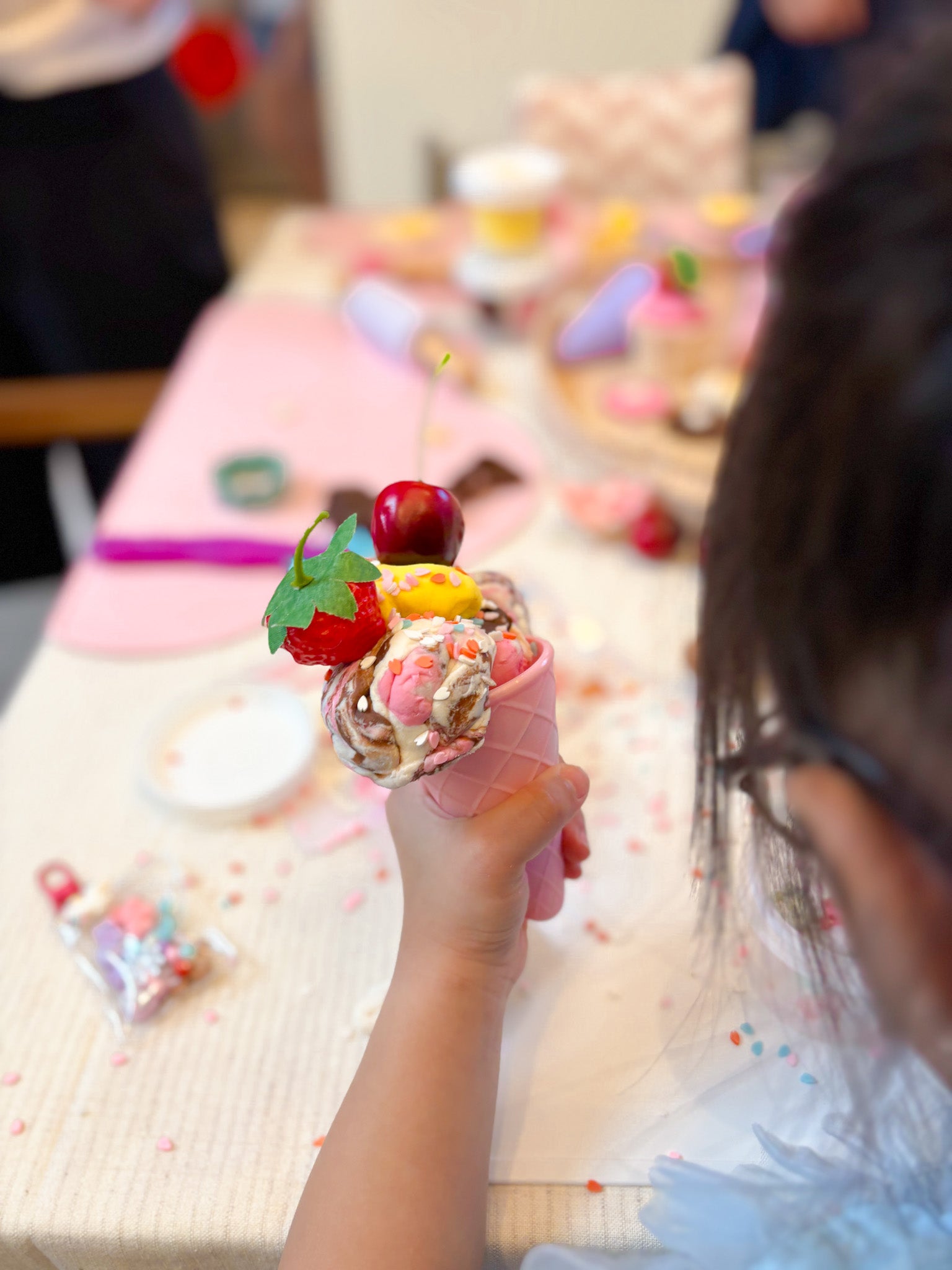 Child's hand holding a decorated playdough ice cream cone at a party.