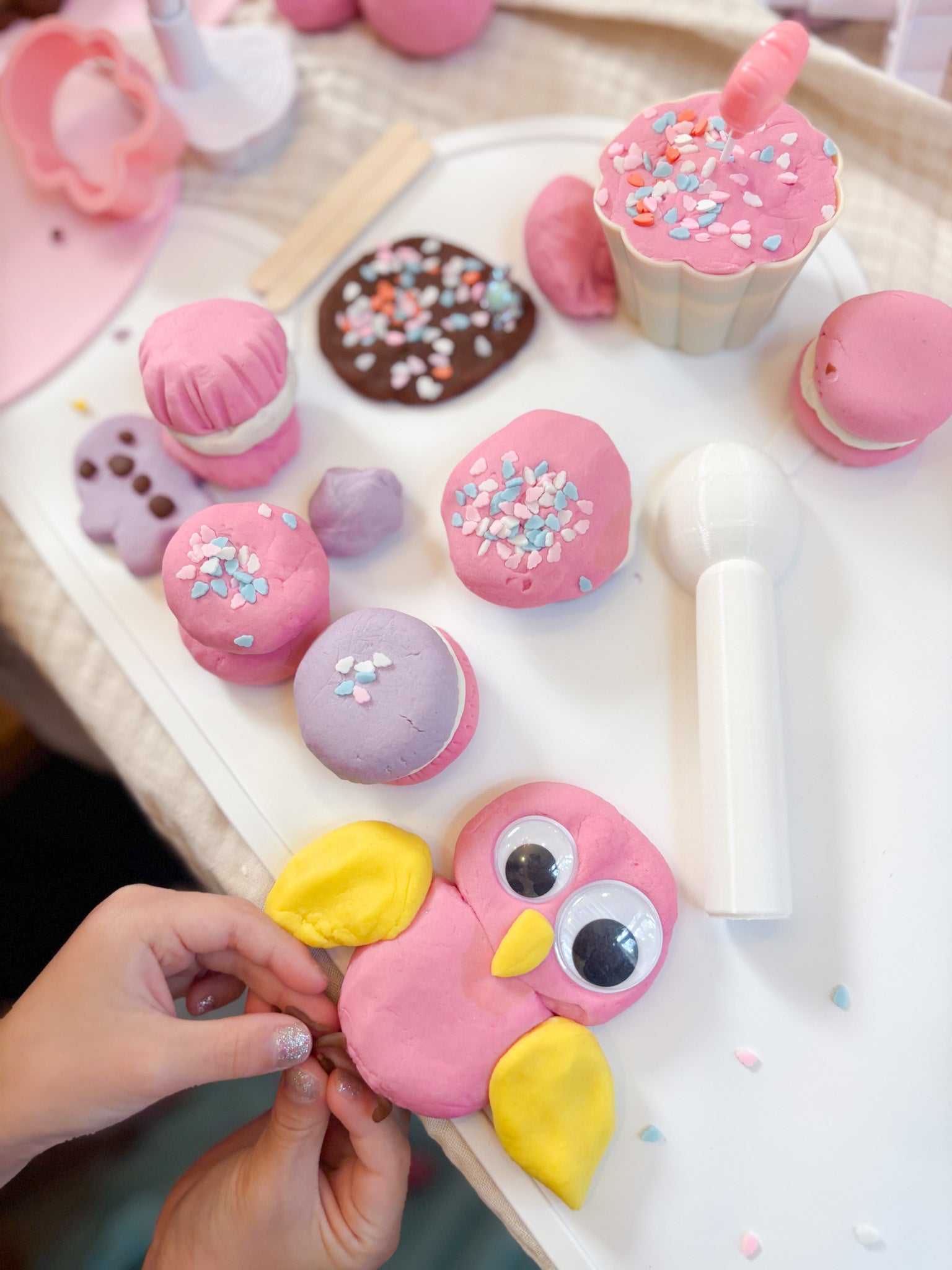 Colorful playdough creations on a tray with a hand holding a pink owl-shaped playdough creation