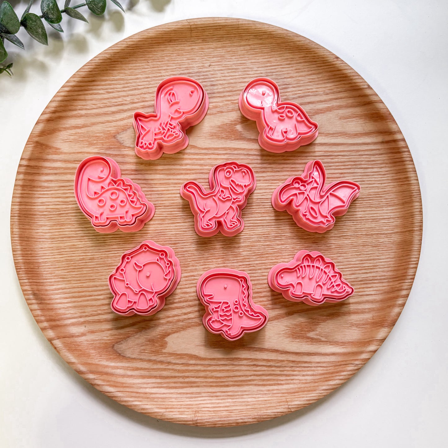 Set of pink dnosaur-shaped cookie cutters on a wooden plate.