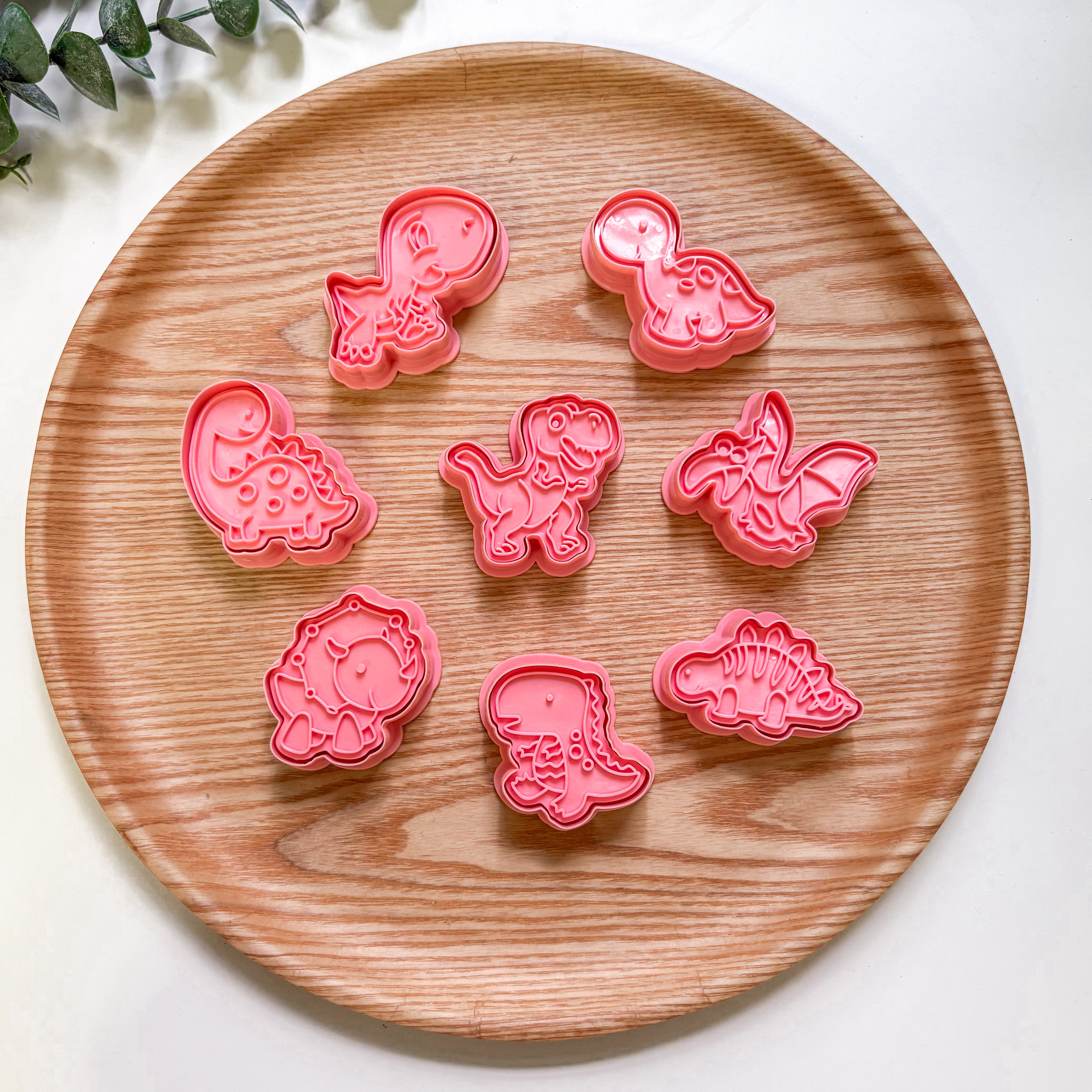 Set of pink dnosaur-shaped cookie cutters on a wooden plate.