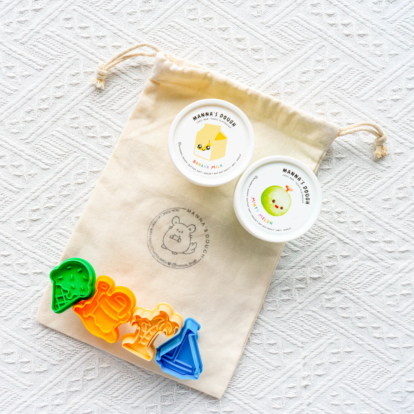 Colorful cookie cutters with a branded drawstring bag on a textured white background