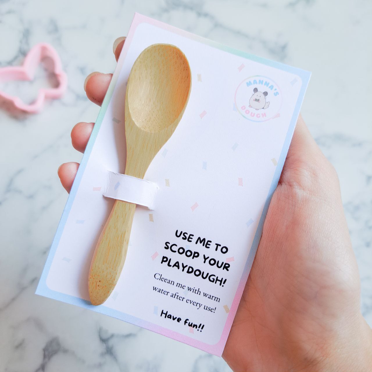 A wooden playdough scoop with a colorful backing