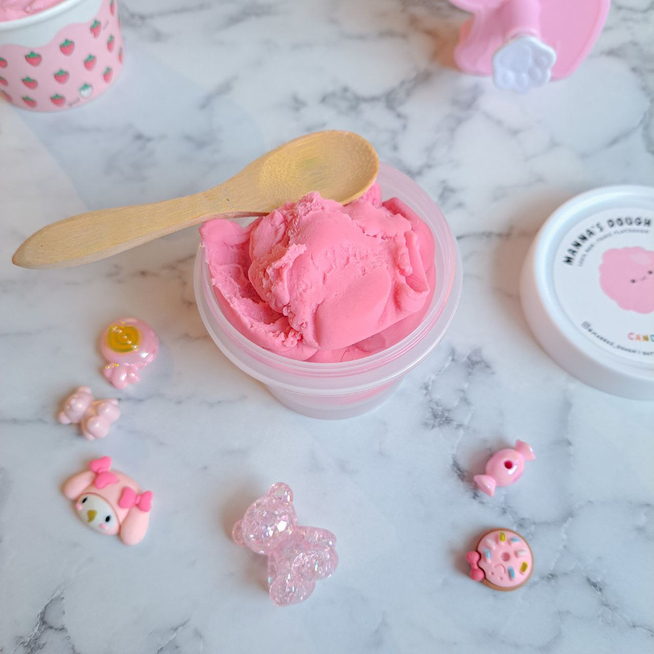 A wooden playdough scoop with a tub of pink playdoughs
