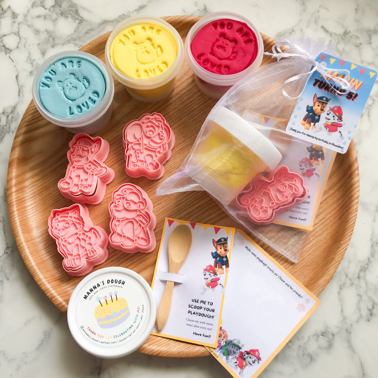 Packaged playdough party packs with Paw Patrol themed decorations, including character cutters and a themed gift tag.
