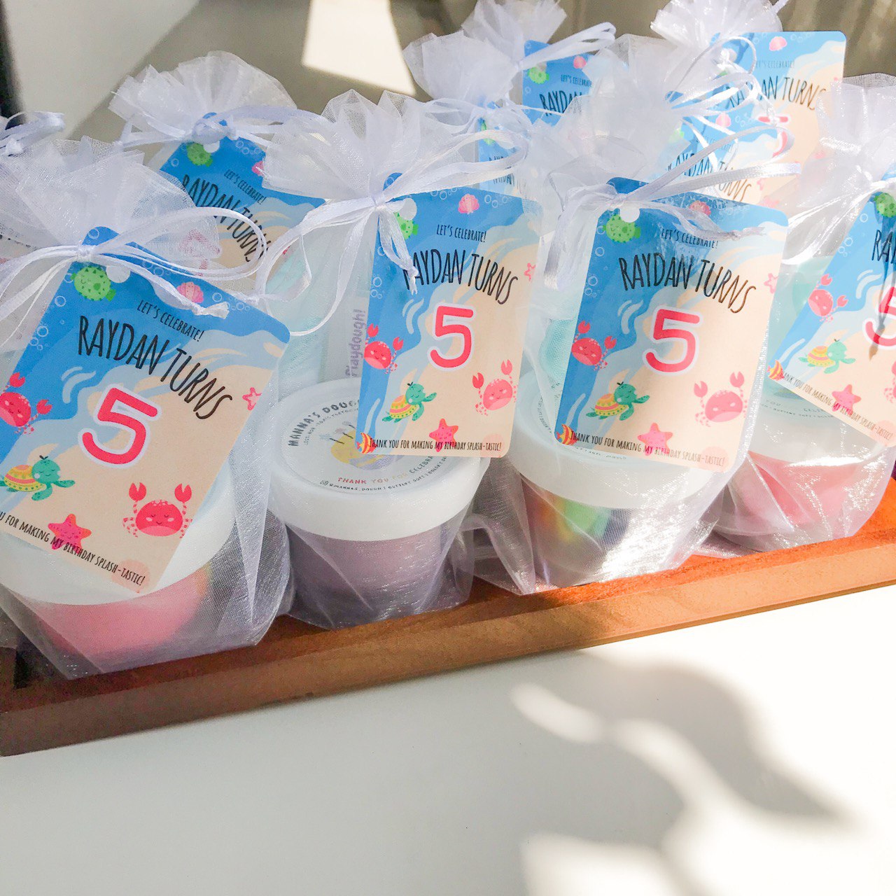 A set of 9 party packs. Each pack contains a playdough tub and a gift tag that is beach themed