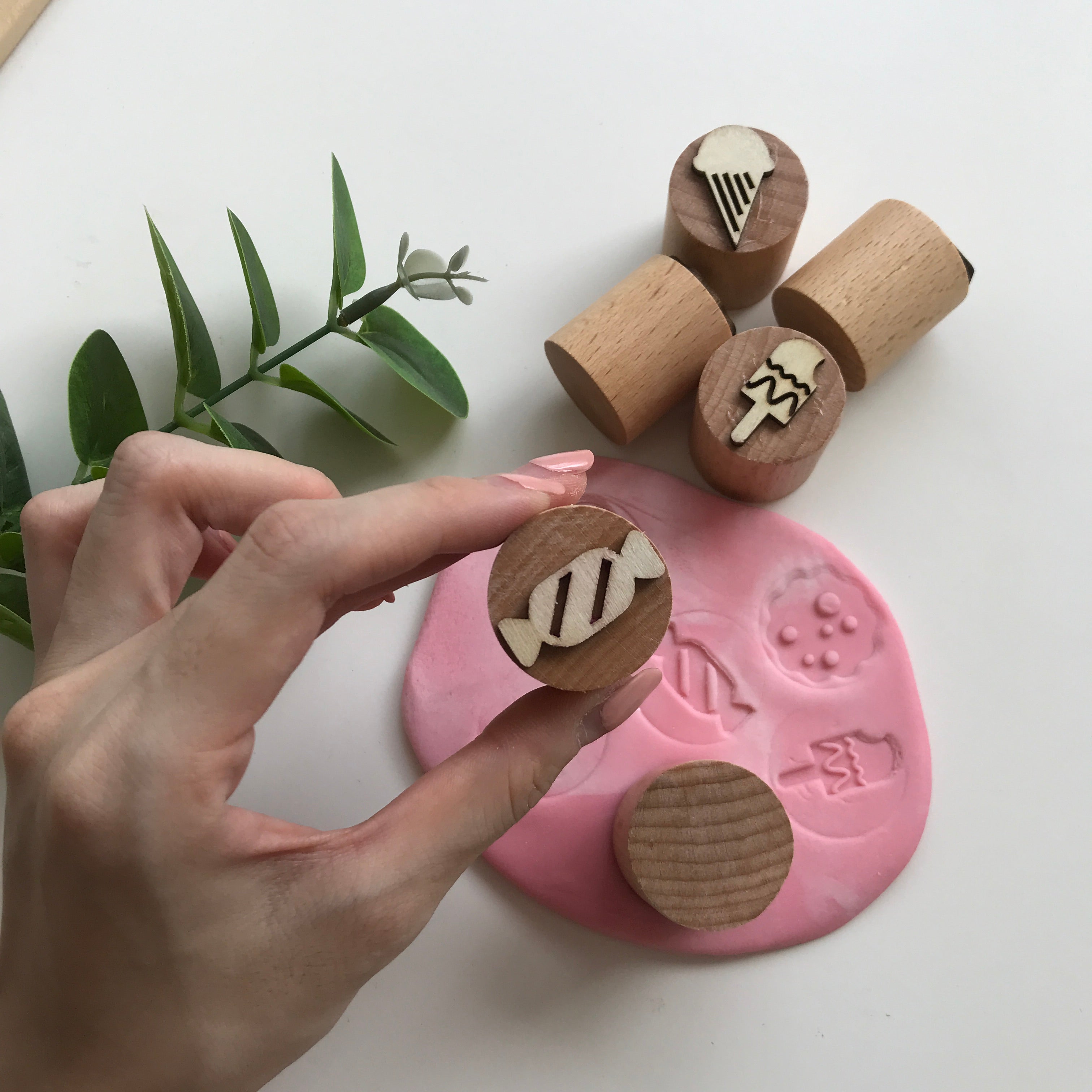 A hand holding up wooden stamp with candy print. Background contains wooden stamps with other sweet treat designs 