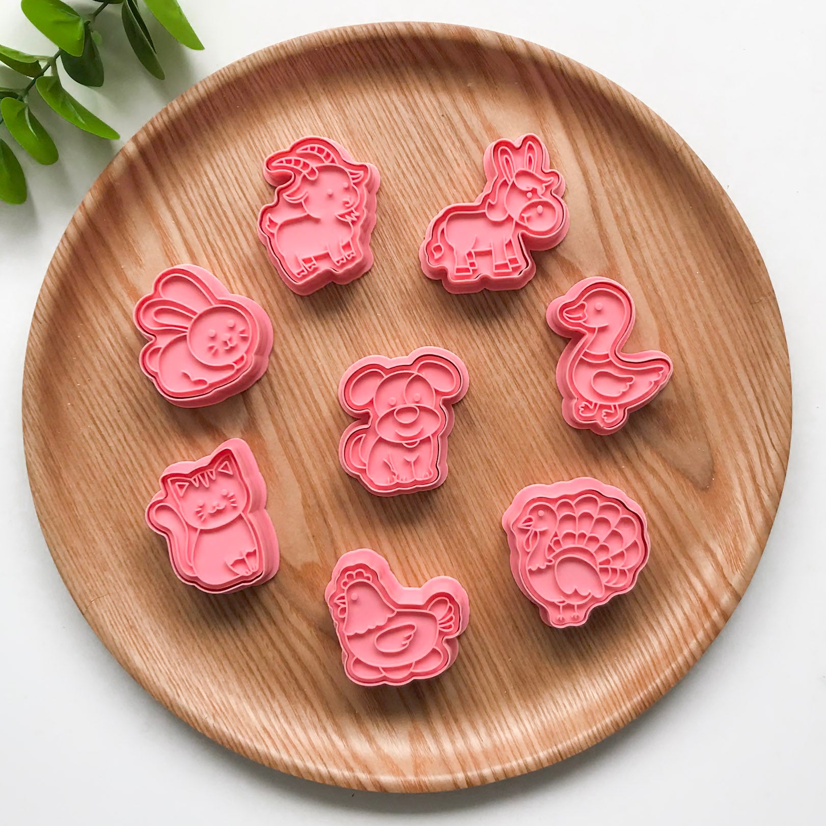 A set of pink animal-shaped cutters on a wooden surface, with a variety of animal figures such as rabbits, chickens, and ducks. There is also a wooden cutter piece with a design of a rabbit.