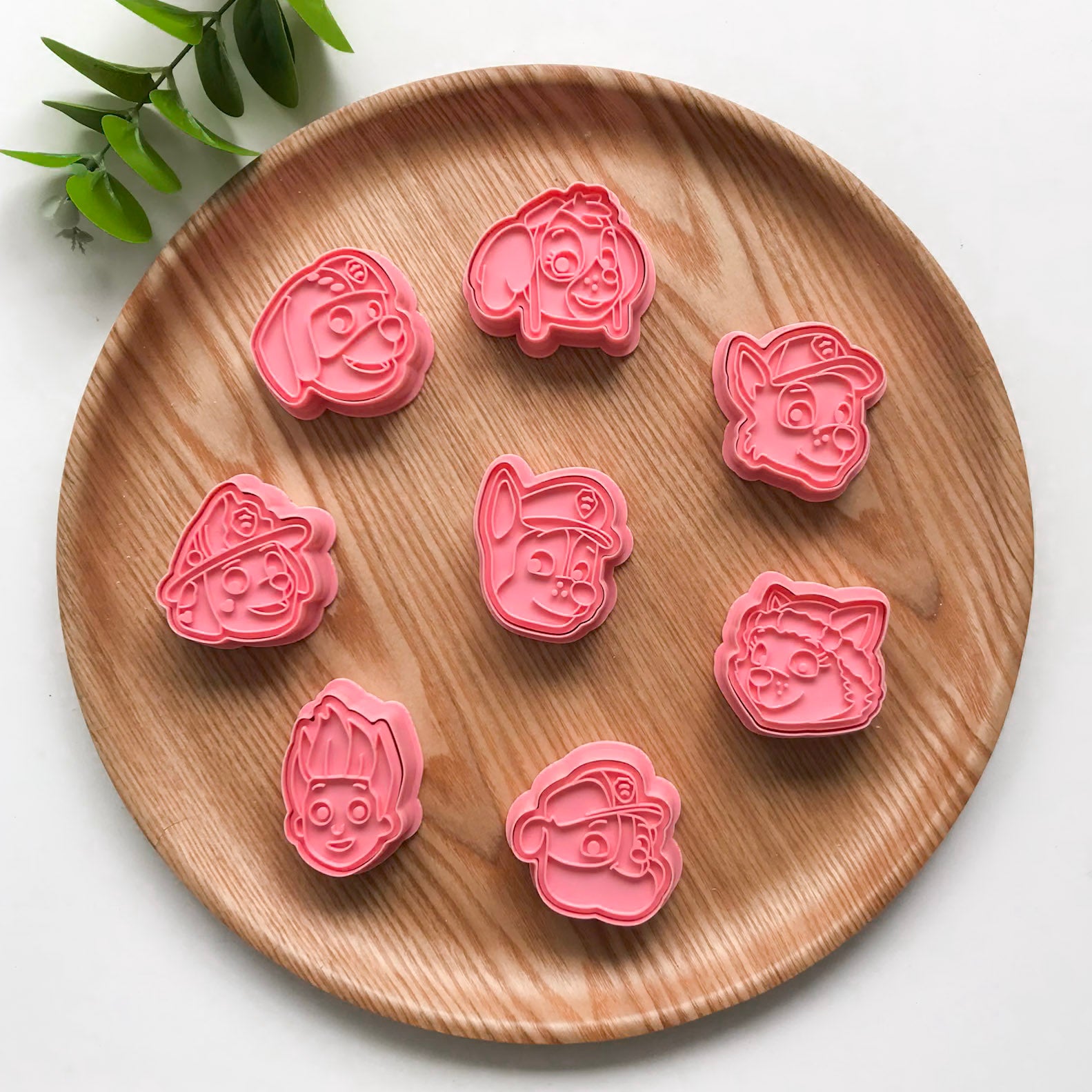 A set of colorful paw patrol face-shaped cutters for crafting, displayed on a wooden plate. Each cutter has a cartoonish puppy face design