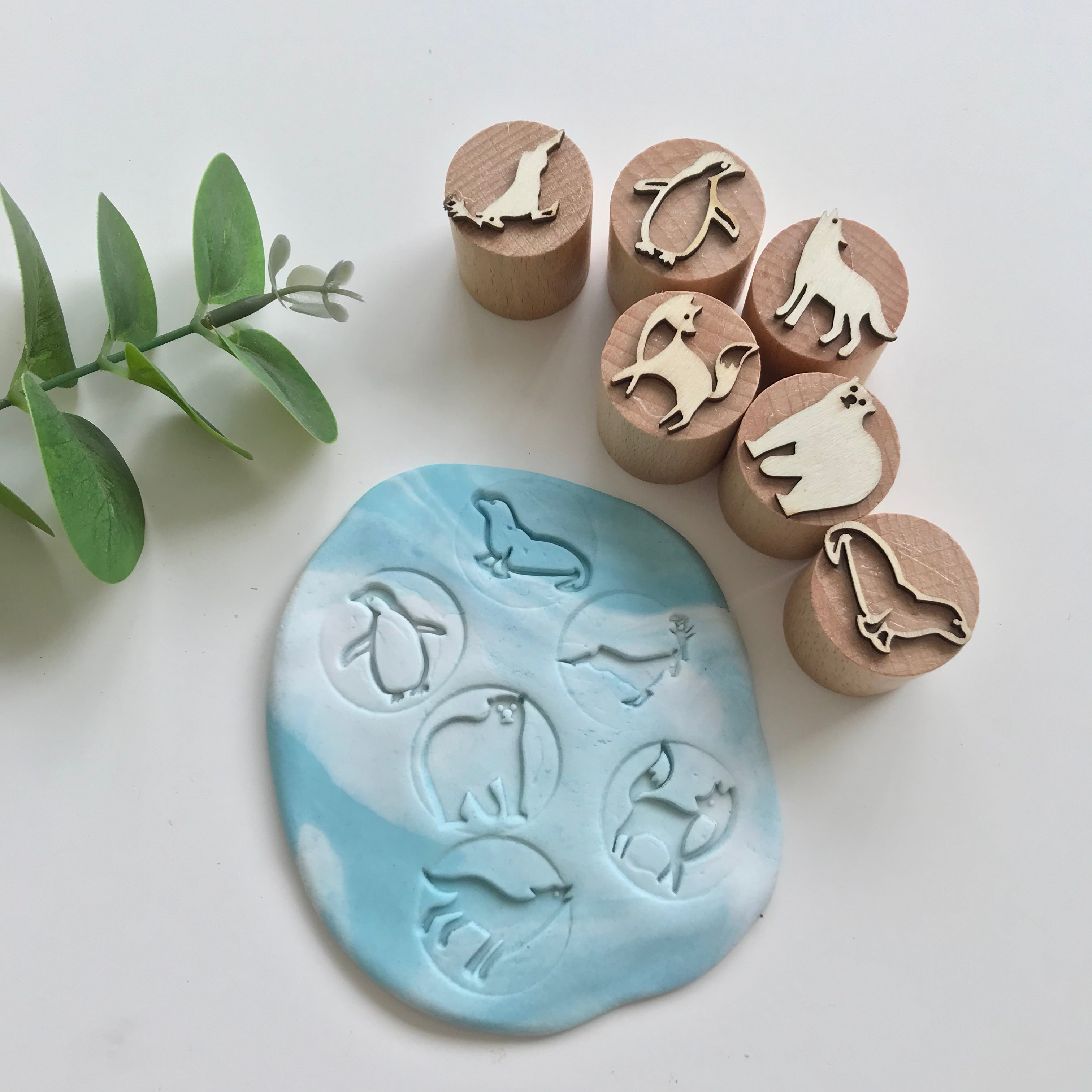 Set of 6 playdough wooden stampers in artic theme alongside their respective imprints on a marbled blue and white playdough