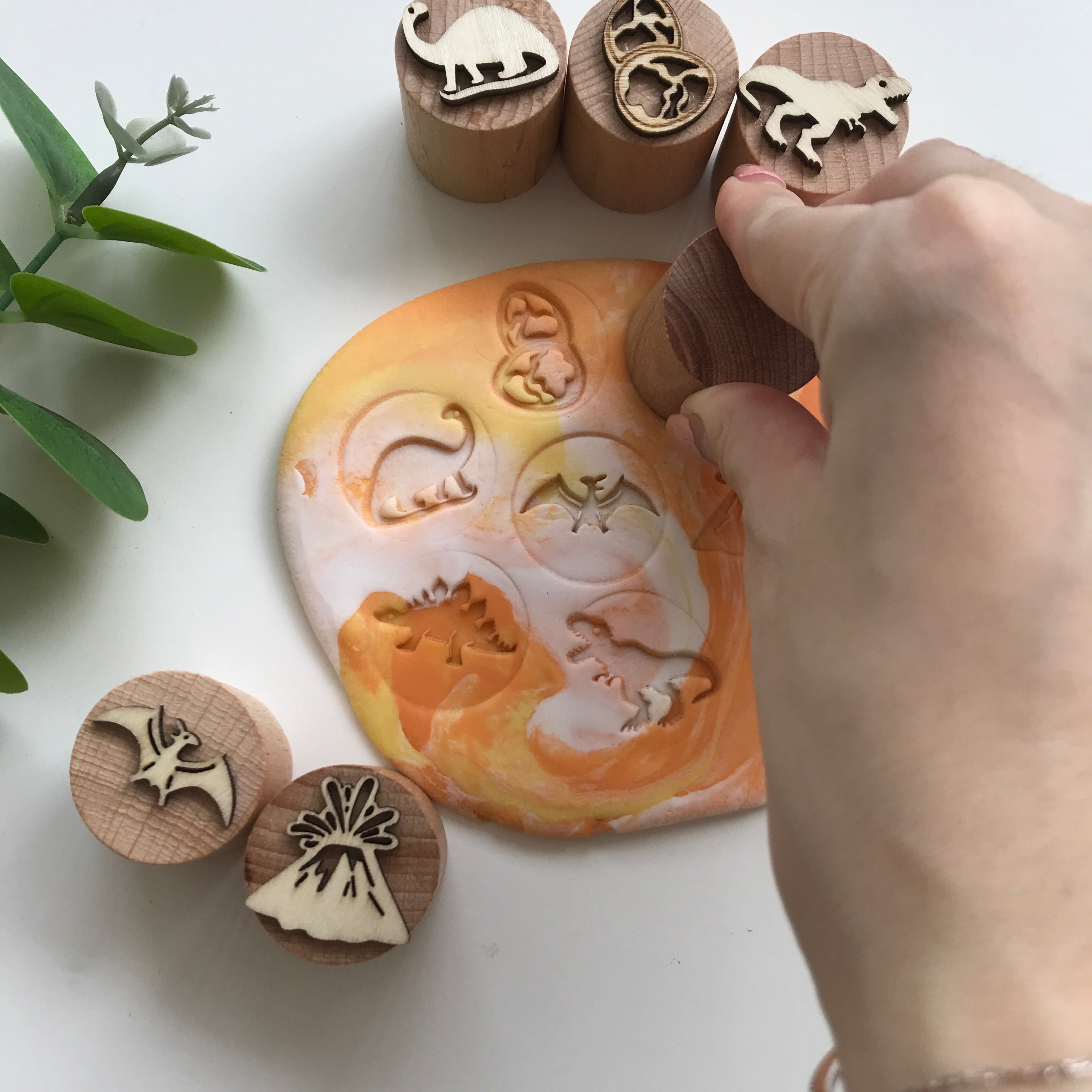 Hand holding a wooden playdough stamp, pressing down against the playdough to make an imprint