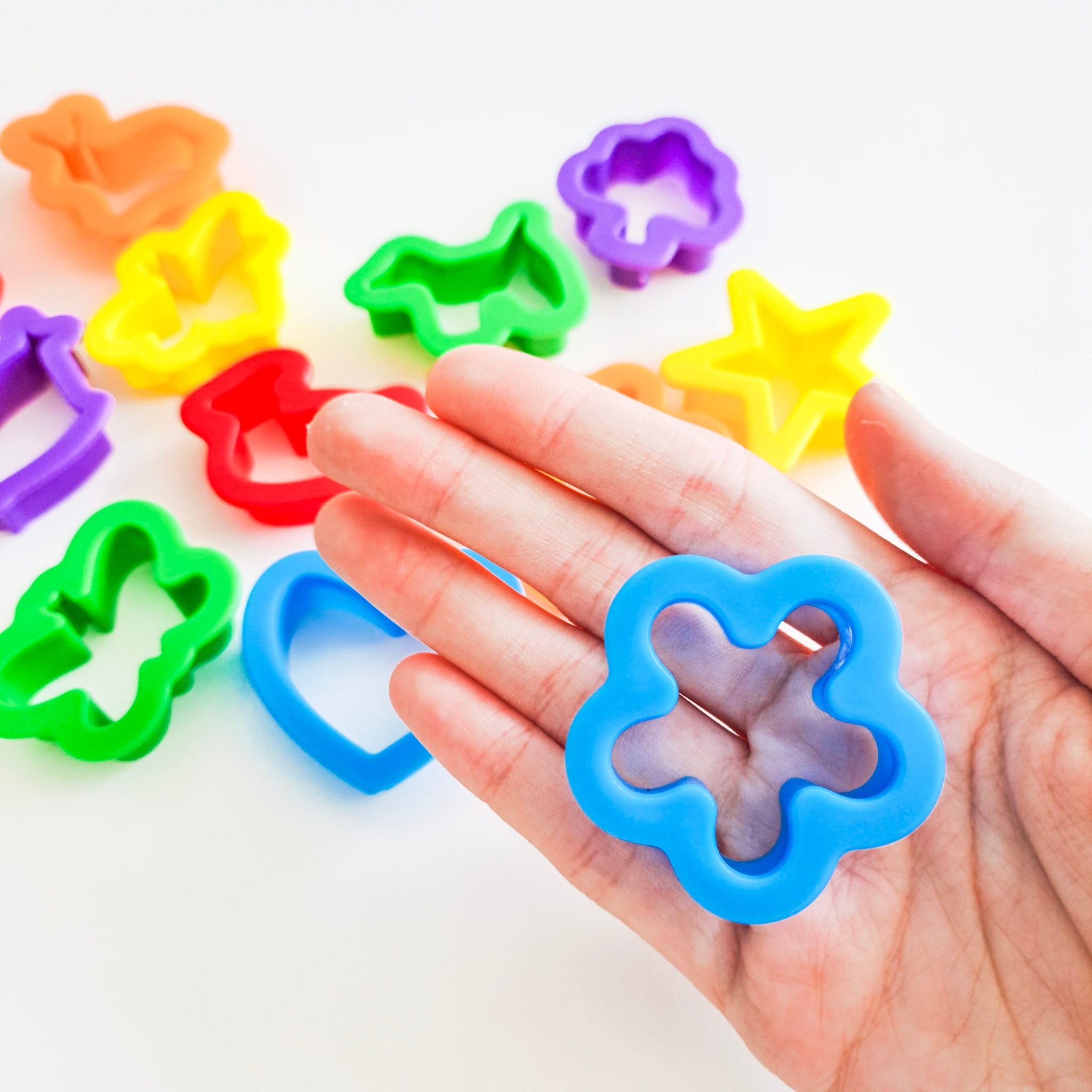A hand holding a colorful plastic cutter with a star shape, alongside other cutters in various colors.
