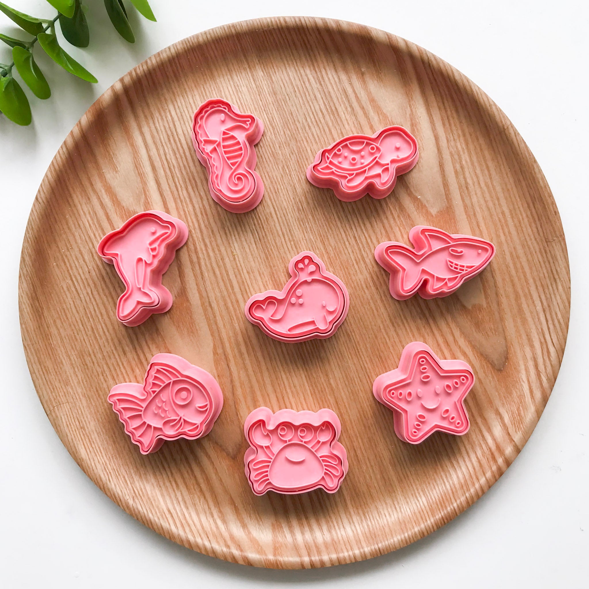 A set of colorful ocean animal-themed playdough cutters displayed on a wooden plate. The animals featured are a turtle, seahorse, dolphin, starfish, whale, crab, shark and a fish