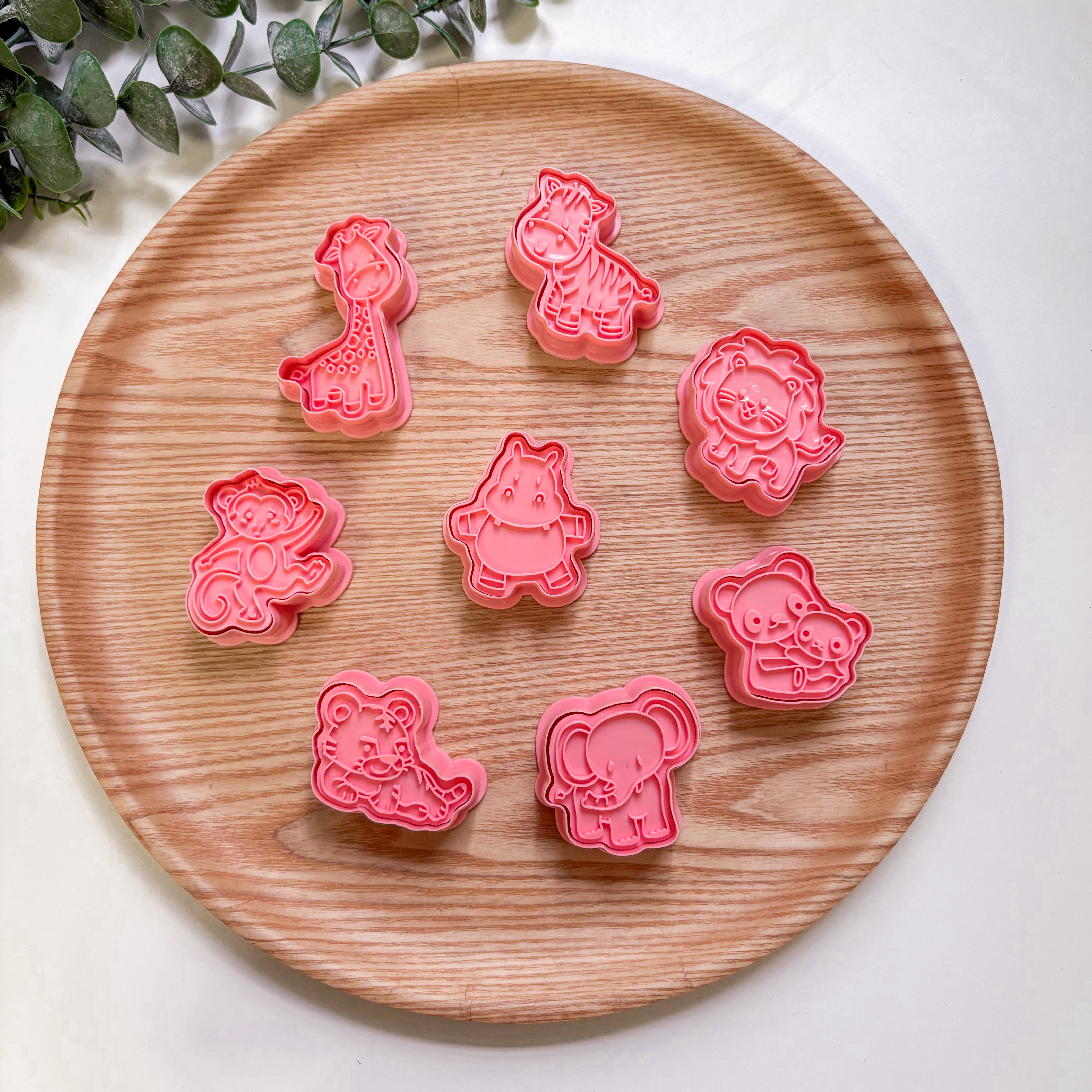 Set of pink animal-shaped cookie cutters on a wooden plate with a white background.