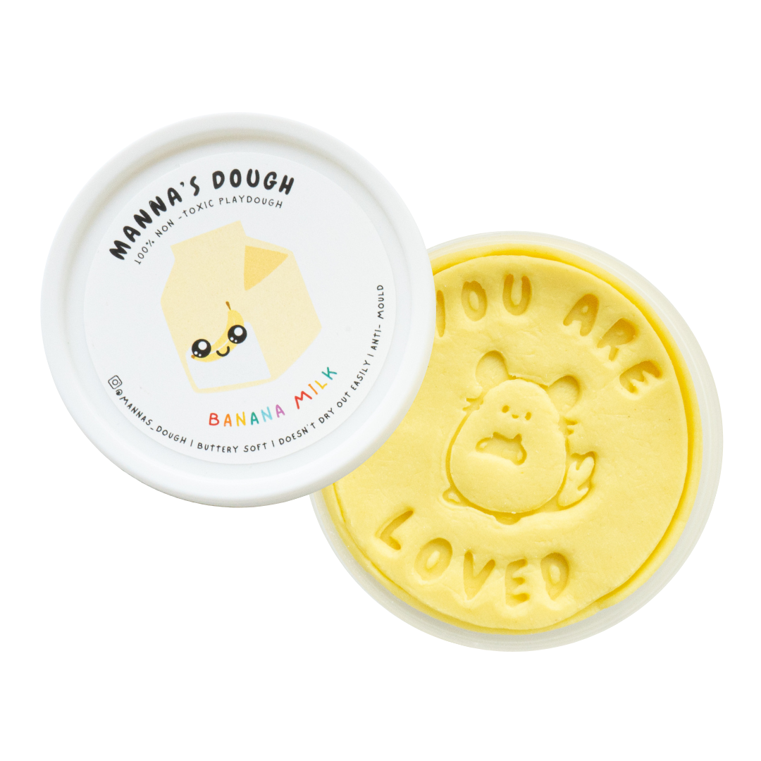 Soft yellow playdough from Manna's Dough, labeled 'Banana Milk' with a cute milk carton design on the lid. The playdough is stamped with 'YOU ARE LOVED' and a charming banana milk character, ideal for fun and creative play.