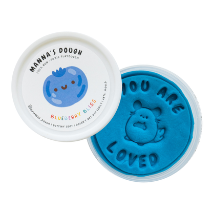 Deep blue playdough from Manna's Dough, labeled 'Blueberry Bliss' with a smiling blueberry design on the lid. The soft, non-toxic playdough is stamped with 'YOU ARE LOVED' and a sweet animal character, perfect for imaginative and safe play