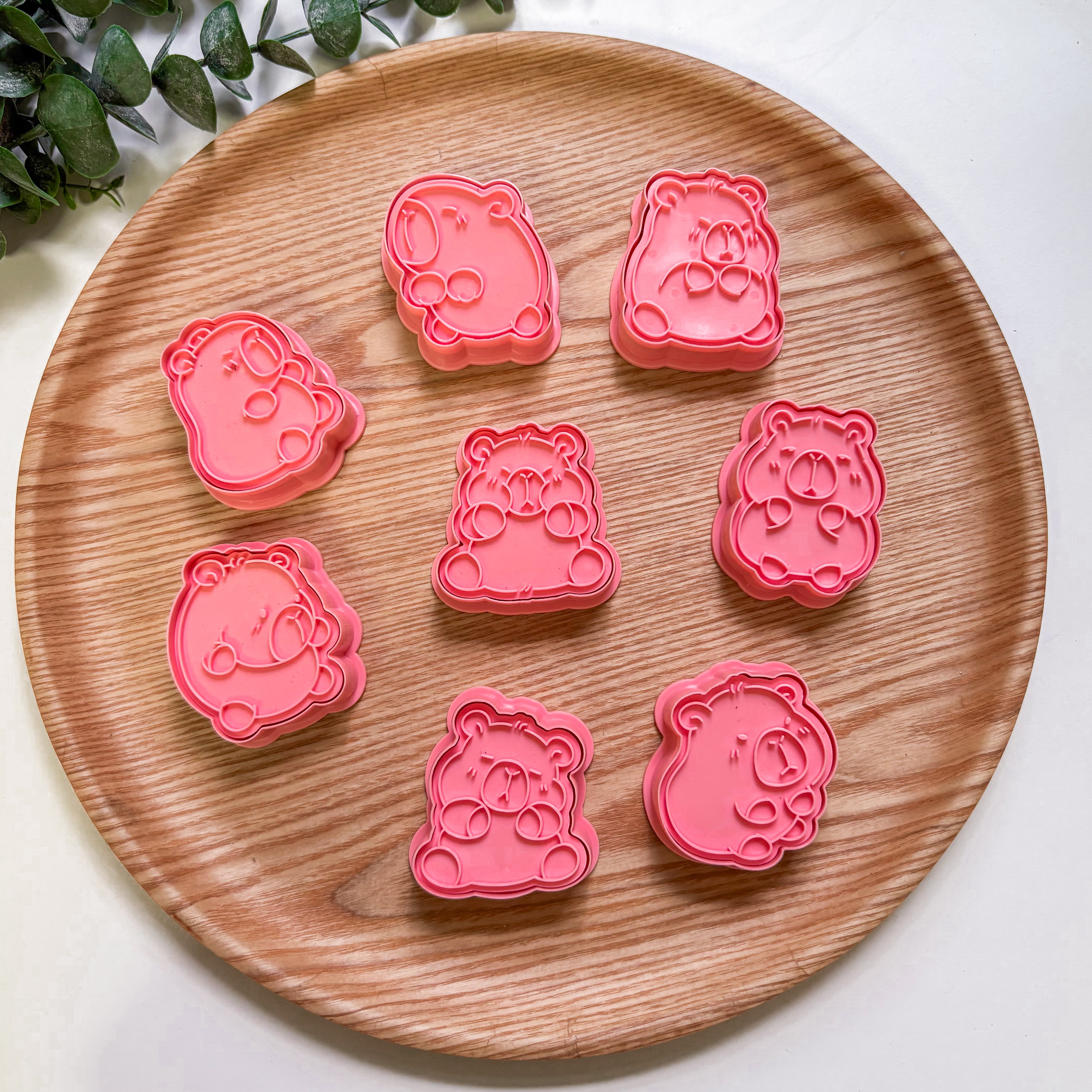 Pink capybara-shaped cookie & playdough cutters on a wooden plate with a white background