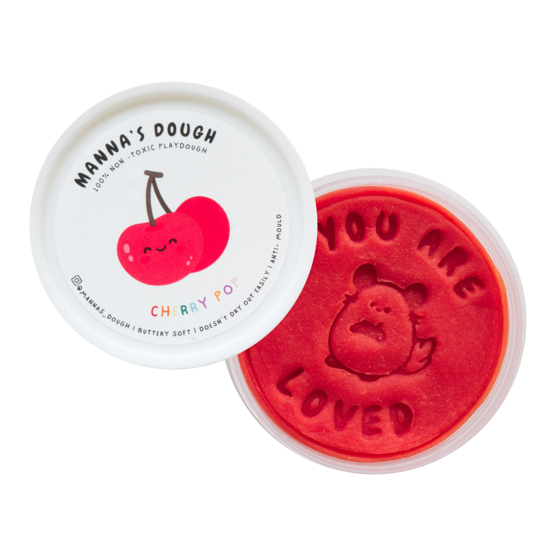 Vibrant red playdough from Manna's Dough, labeled 'Cherry Pop' with a cheerful cherry design on the lid. The soft, non-toxic playdough is stamped with 'YOU ARE LOVED' and a cute cherry character, ideal for safe and creative playtime.