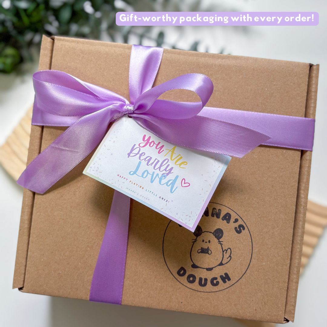 Brown box with a purple ribbon and a tag, featuring a brand logo, on a blurred green background.