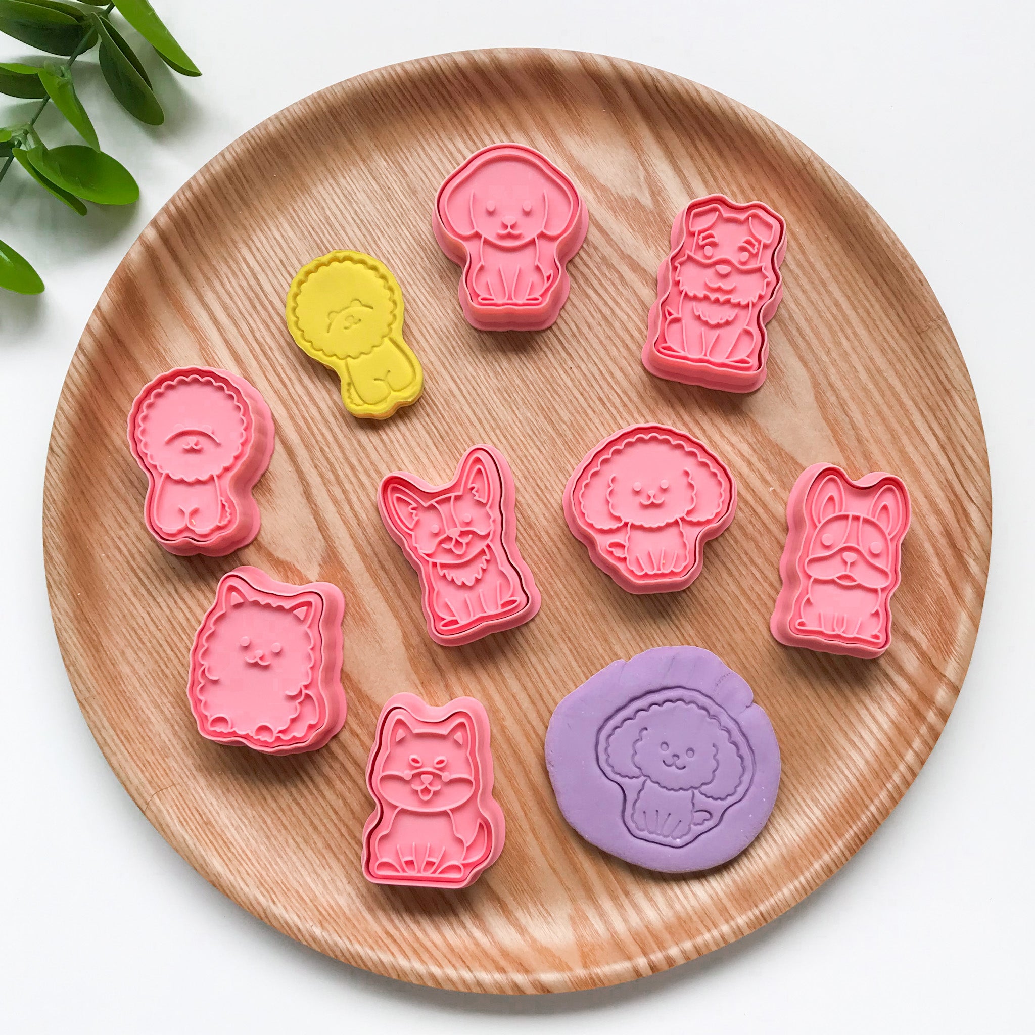A collection of pink-colored Dog themed playdough cutters arranged on a wooden plate. Features 8 different breeds of dogs
