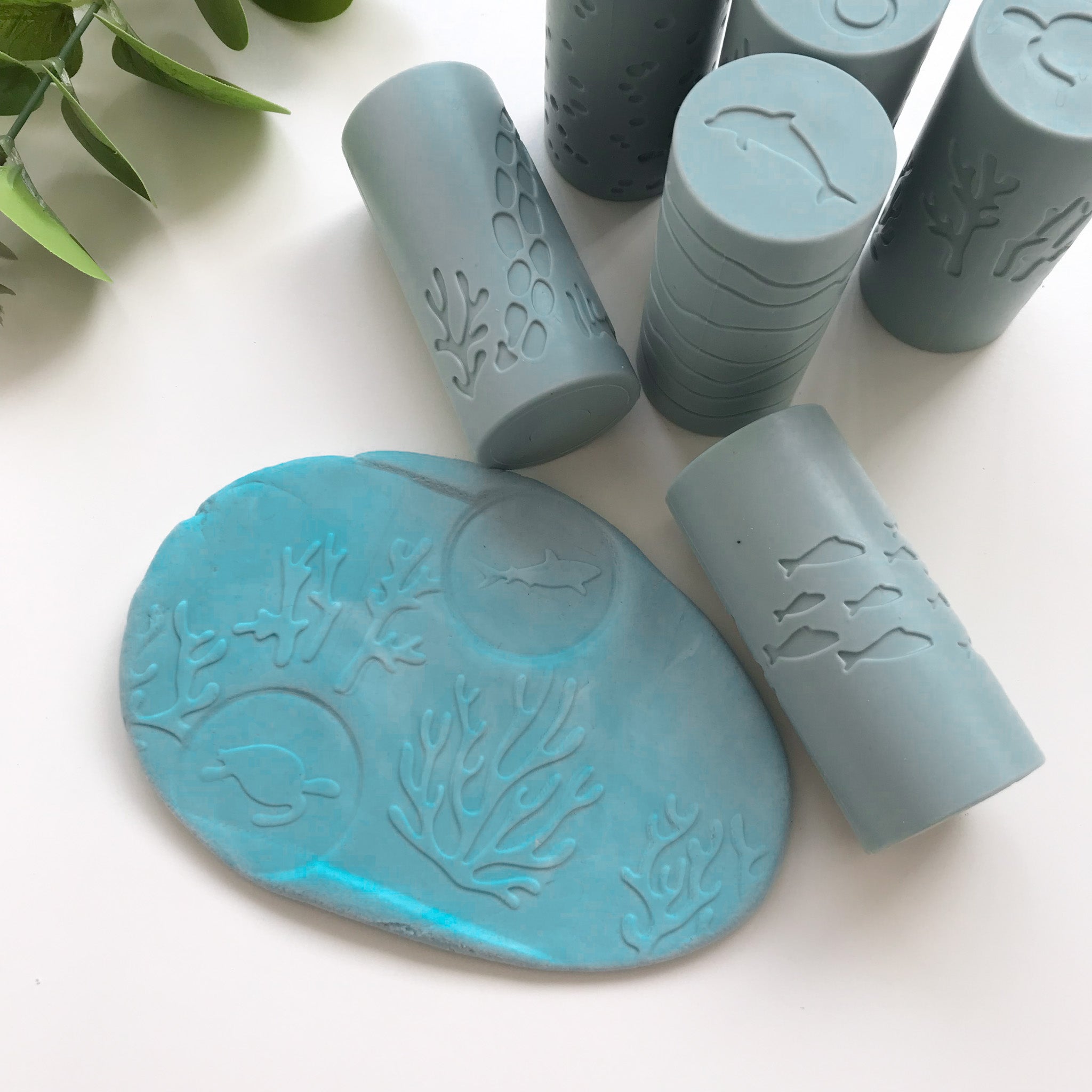 A set of silicone playdough rollers with assorted prints along with a flat piece of blue playdough that has coral and turtle and a shark stamped on it
