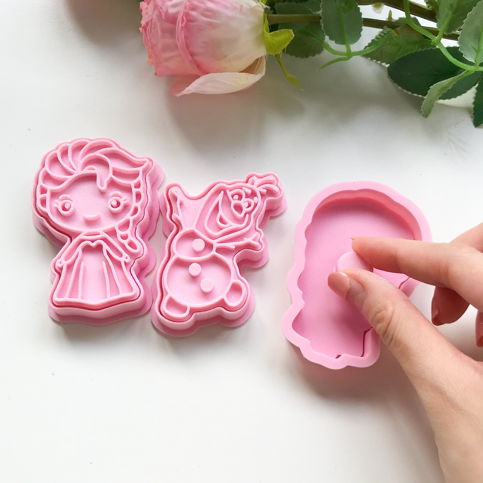 A set of 3 frozen themed playdough cutters. Elsa, Olaf and Anna. There is a hand grasping on the Anna cutter to demonstrate how to use the cutters