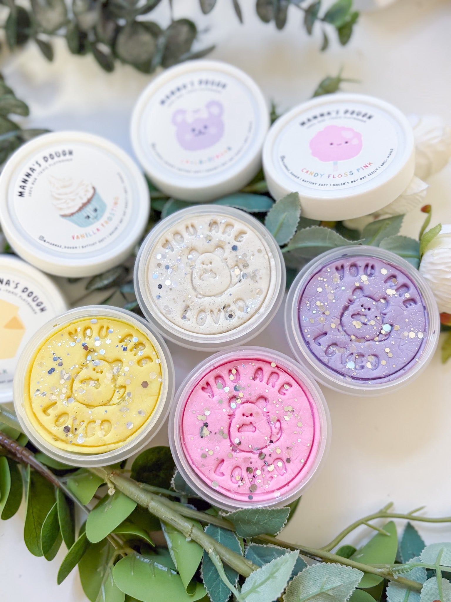 Glitter playdoughs in the colors lilac, white, yellow and pastel pink. Set against a lush green backdrop