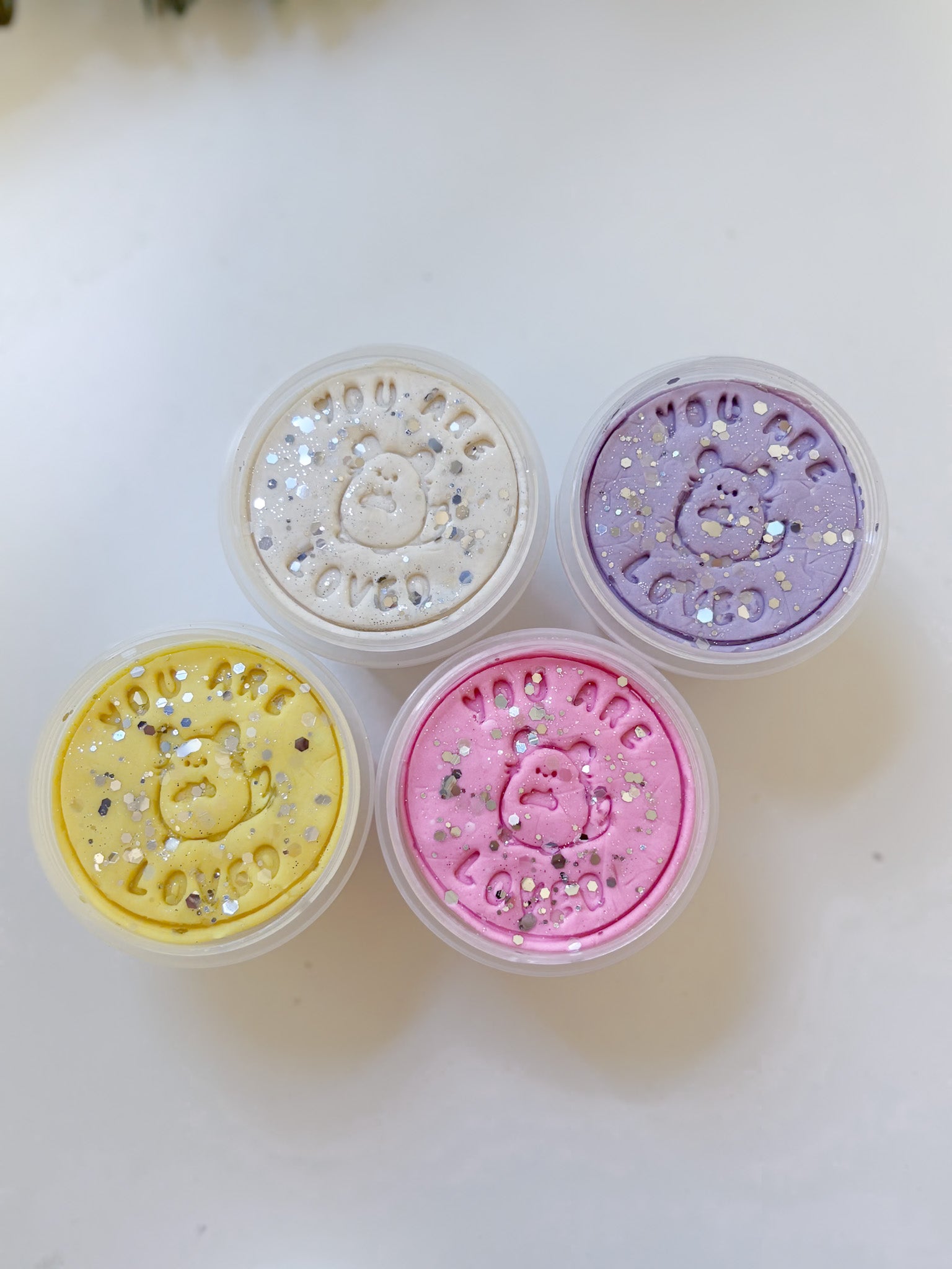 Glitter playdoughs in the colors lilac, white, yellow and pastel pink. Set against a white backdrop