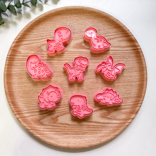 Set of pink dnosaur-shaped cookie cutters on a wooden plate.