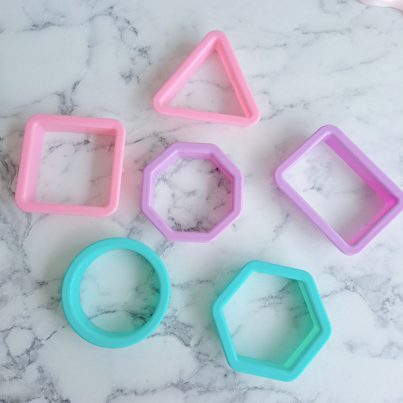 A set of colorful playdough cutters in various shapes placed on a marble surface.