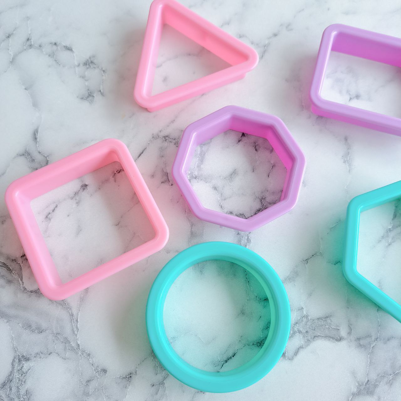 A set of colorful playdough cutters in various shapes placed on a marble surface.