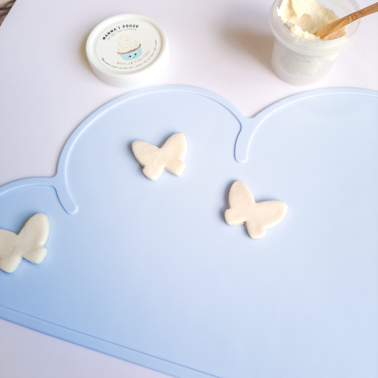 Blue silicone mat along with a tub of white playdough and 3 butterfly cutouts