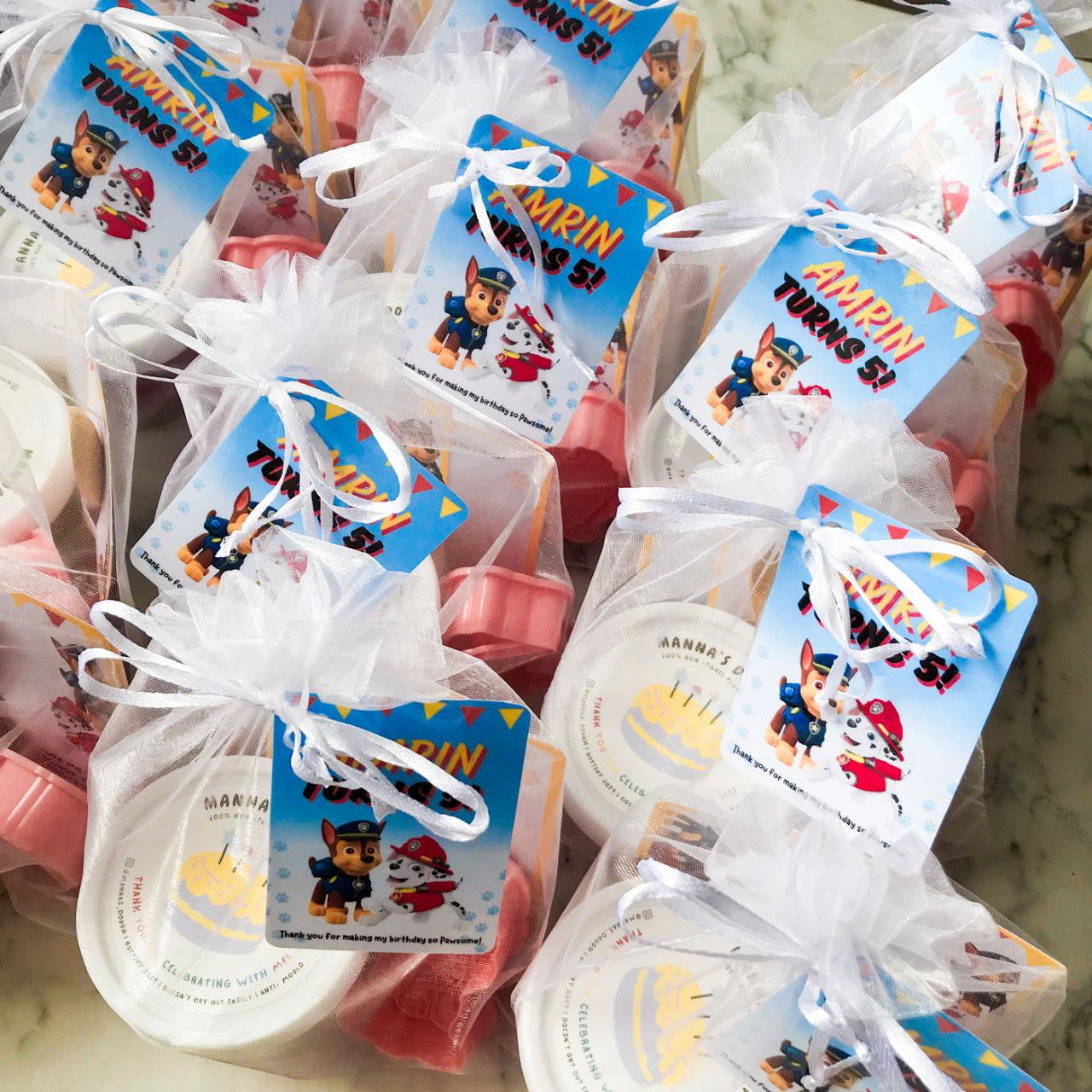 Packaged playdough party packs with Paw Patrol themed decorations, including character cutters and a themed gift tag.